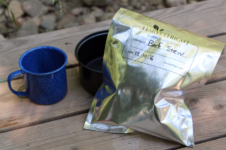 A camping mug and a bag of freeze dried food in a mylar bag on a wooden table