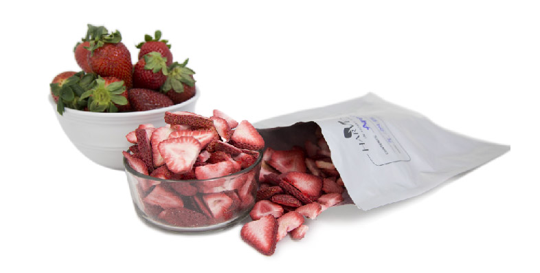 A white bowl of fresh strawberries, a clear bowl of freeze dried strawberries, and a mylar bag of freeze dried strawberries, on a bright white background